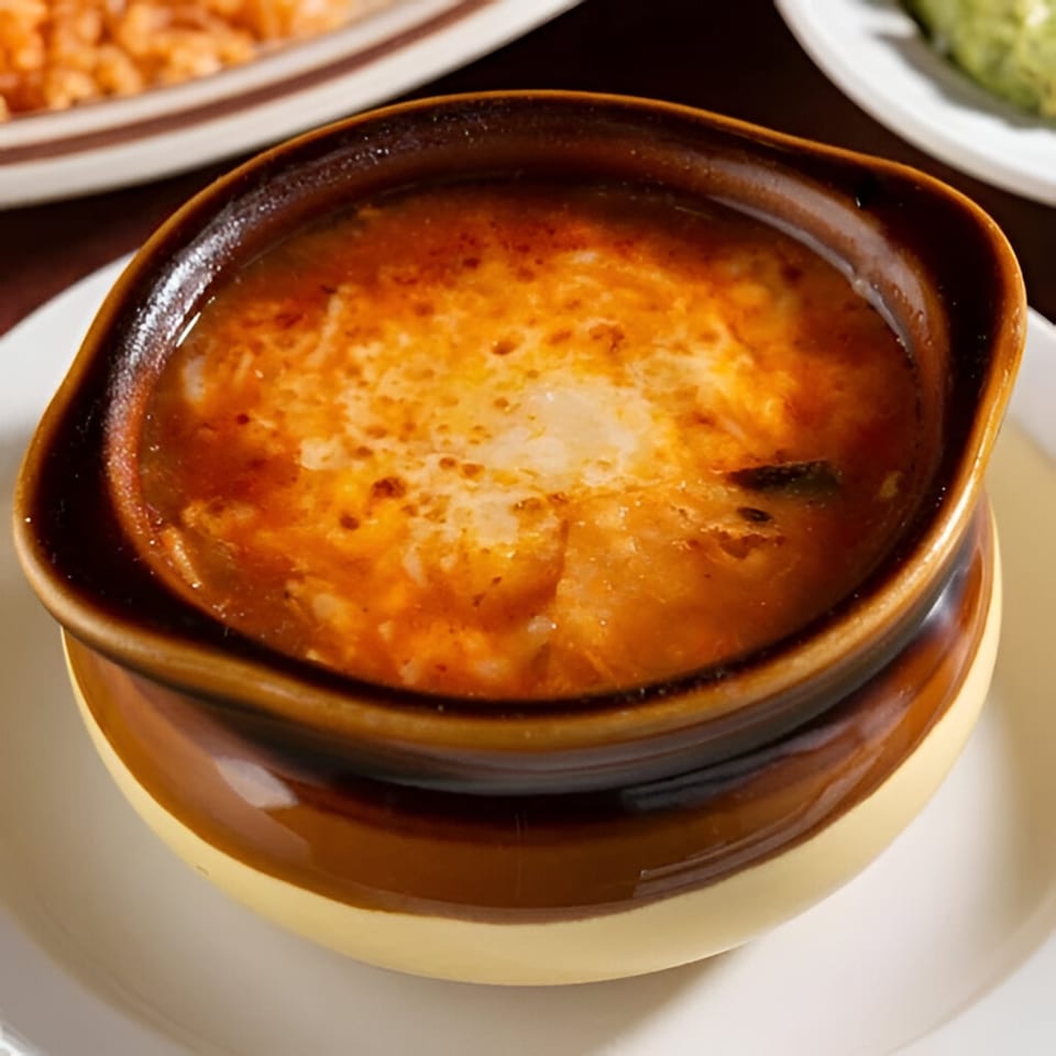 A brown ceramic bowl filled with a rich, orange-red Mexican soup topped with melted cheese.