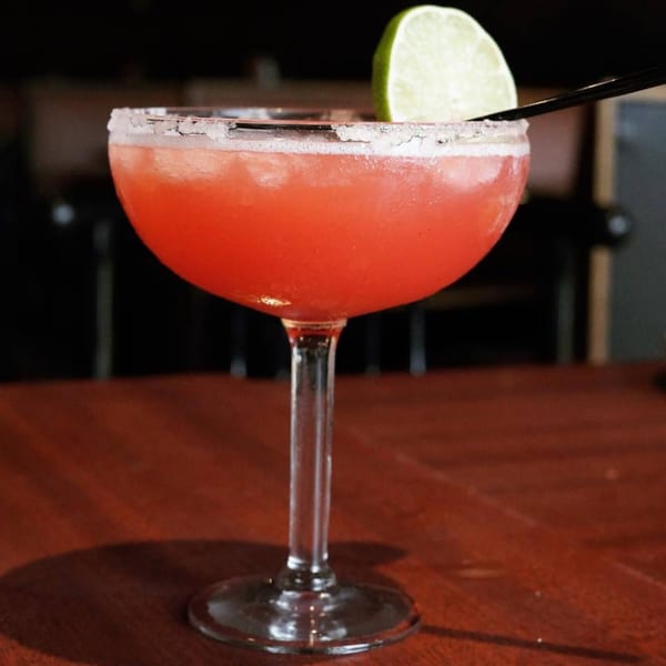A vibrant red margarita with a salted rim, lime wedge, and straw sits on a wooden table.