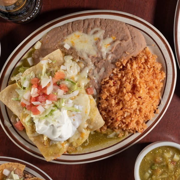 Pancho Villa's enchiladas with green sauce, topped with lettuce, tomato, onion, and sour cream, served with rice and beans.