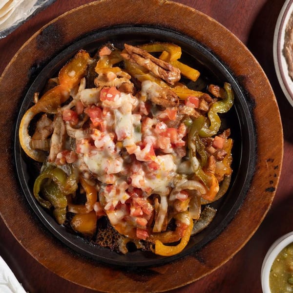 Sizzling fajitas with chicken, bell peppers, onions, melted cheese, and diced tomatoes in a cast iron skillet.