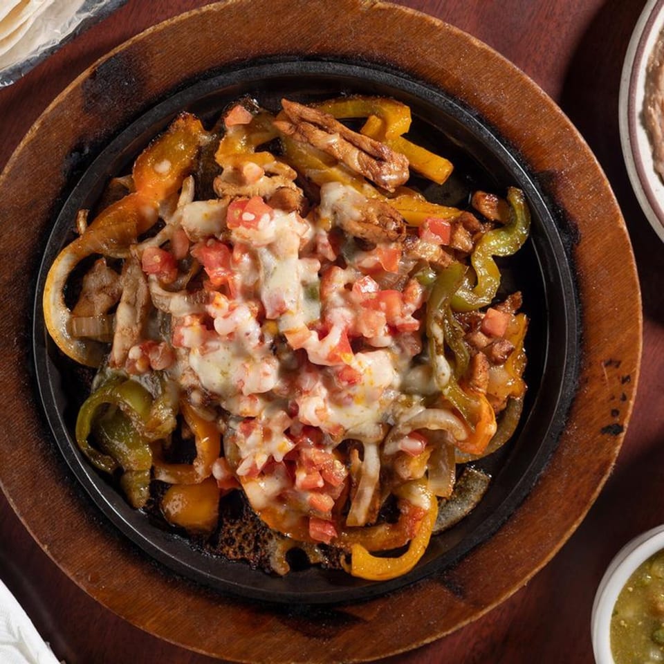 Sizzling fajitas with chicken, bell peppers, onions, melted cheese, and diced tomatoes in a cast iron skillet.
