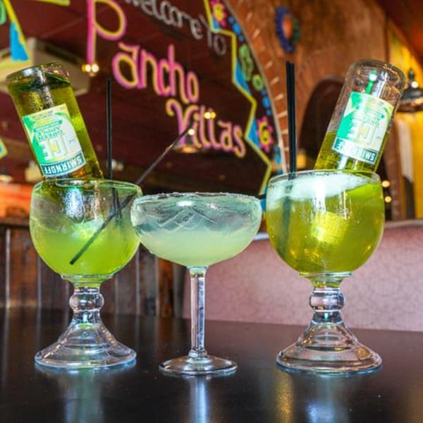 Two large green margaritas with inverted Smirnoff Ice bottles and one smaller margarita on a bar.