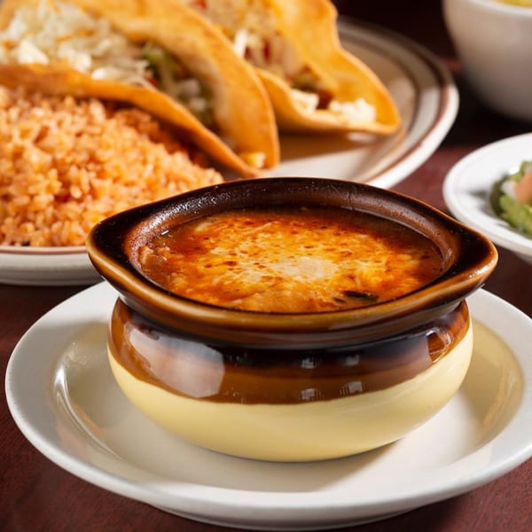 A bowl of melted cheese dip with tacos and rice in the background at Pancho Villa's.