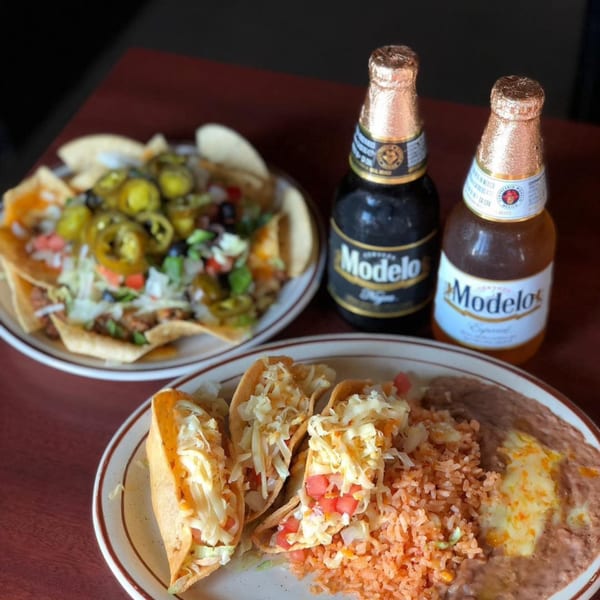 Plates of Pancho Villa's Mexican tacos, nachos, rice, beans, and two Modelo beer bottles.