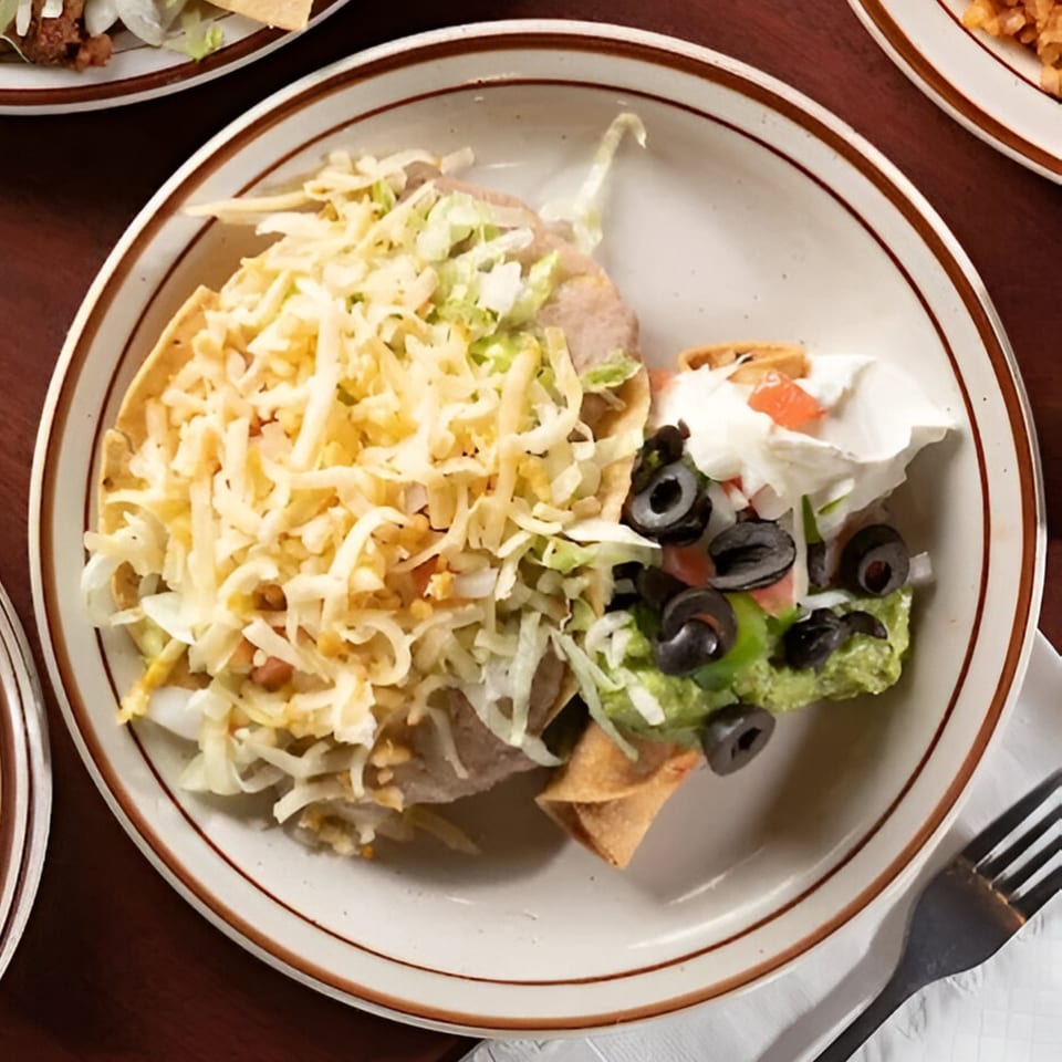 A Pancho Villa's Mexican combo plate with a tostada, taquitos, guacamole, sour cream, and olives.