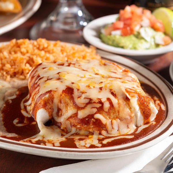 A cheesy enchilada with red sauce, rice, refried beans, and guacamole with pico de gallo.